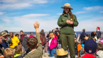 Park ranger in green suit and hat addressing a crowd of visitors