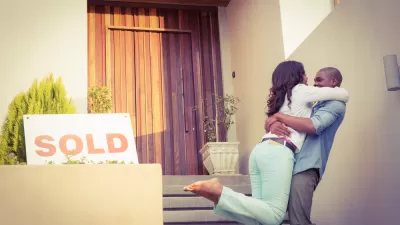 Couple embracing happily in front of home with "SOLD" sign