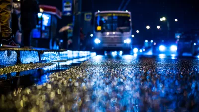 Rainy night in the big city, people standing at the bus stop waiting for the bus. View from the level of asphalt, in blue tones