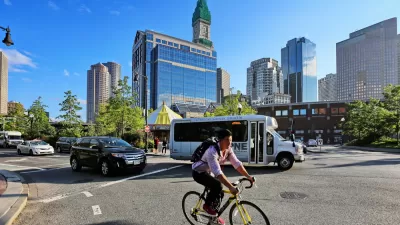 Person on bike wearing backpack with small bus and Boston buildings in background