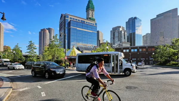 Person on bike wearing backpack with small bus and Boston buildings in background 