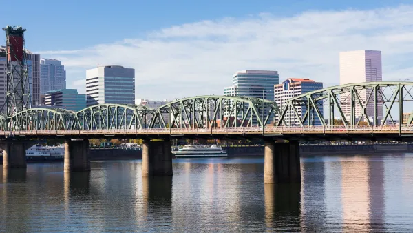 Green steel bridge over Columbia River with Portland, OR skyline in background.