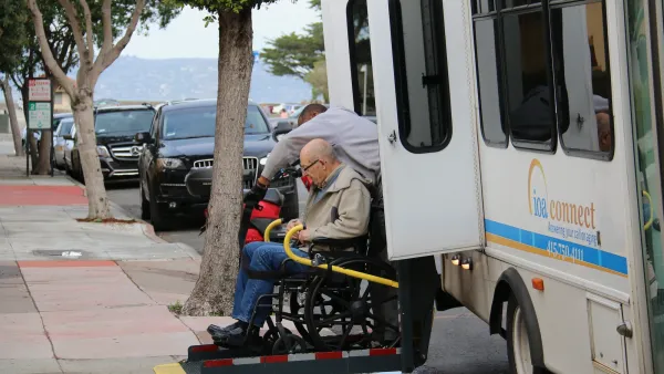 Elderly man in wheelchair exiting white paratransit vehicle.