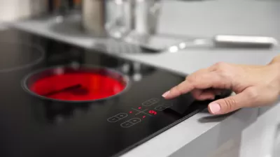 Close-up of black electric stove with red heated coil and person reaching out to press button