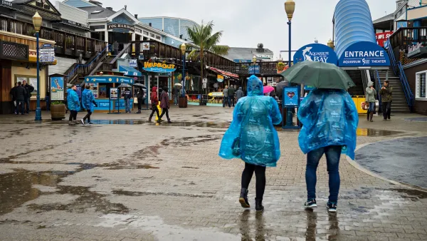 tourists in blue raincoats walk on Pier 39 in the rain in San Francisco.