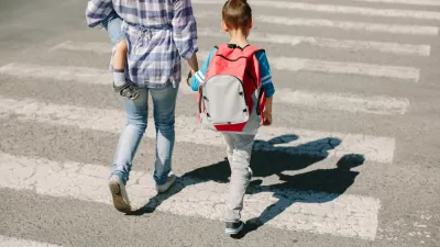 Adult holding small child and holding hand of older child walking across crosswalk