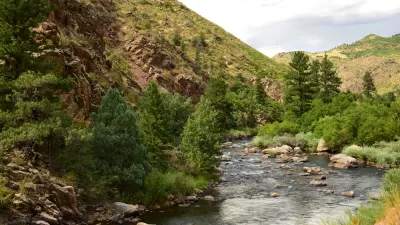 Shallow river with tree-lined banks and hillsides in the background