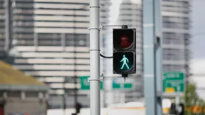 Pedestrian stoplight with green 'walk' silhouette lit up and blurry city buildings in background