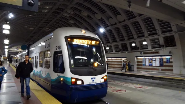 Blue and white Sound Transit light rail train at platform in covered station with man walking towards camera in Seattle, Washington.