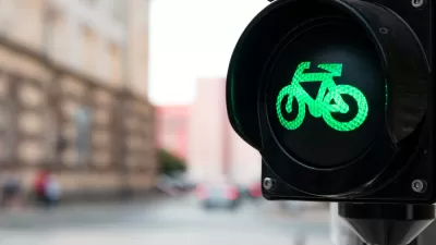 Close-up of black traffic light with green bike symbol lit up and blurry urban scene in background