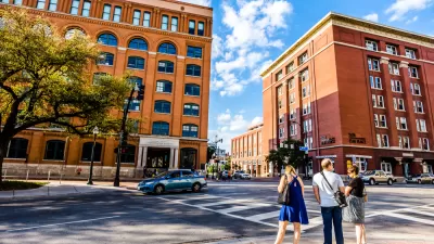 View of Dealey Plaza with pedestrians at crosswalk and brick book depository building in background