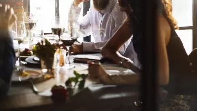 Blurry close-up of people eating at restaurant table with white wine glass in middle