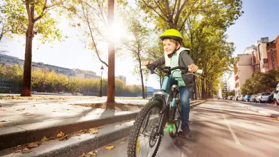 Young boy wearing yellow helmet riding a bicycle down a city street
