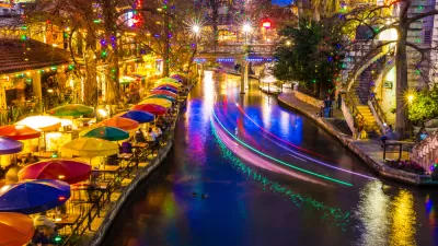 View of San Antonio River Walk with colorful umbrellas at tables on waterfront and with boat lights blurred by long-exposure