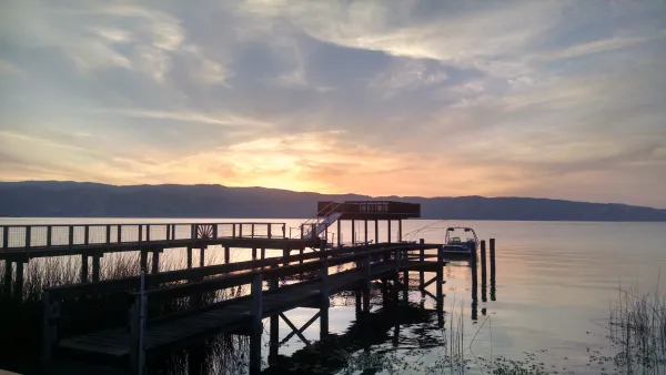 A sunrise over clear lake. A dock extends into the lake, and there are hills in the distance.