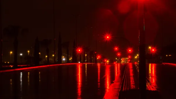 Red street lights on dark, wet-looking road at night.