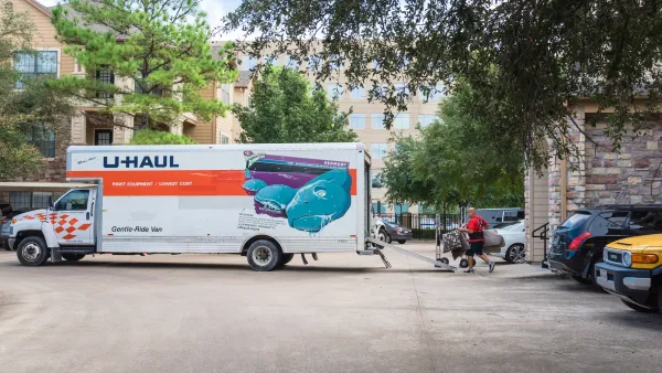 U-Haul moving truck parked perpendicularly in street with man moving furniture into it.