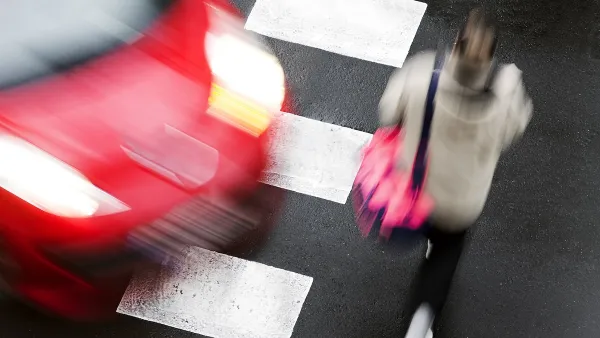 Red car turning into crosswalk as a person walks in front of it.