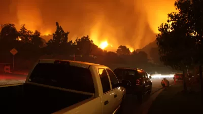 Cars lined up on a street with fire burning in background