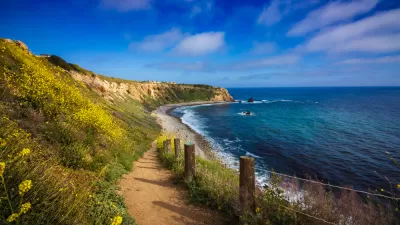 Dirt walking trail with blue ocean on one side and green hillside on the other in Rancho Palos Verdes, California