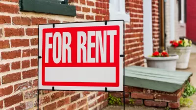 Red and white For Rent sign in front of brick building with flowerpots in background