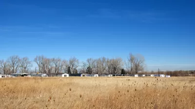 Trailer park and line of bare winter trees in the distance over a golden field on the Colorado prairie.