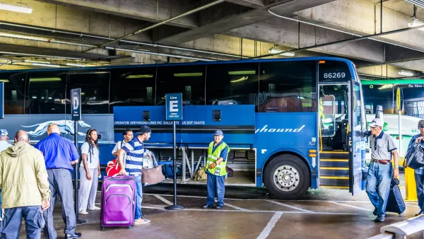 Blue Greyhound bus in a terminal with people with luggage standing next to it.