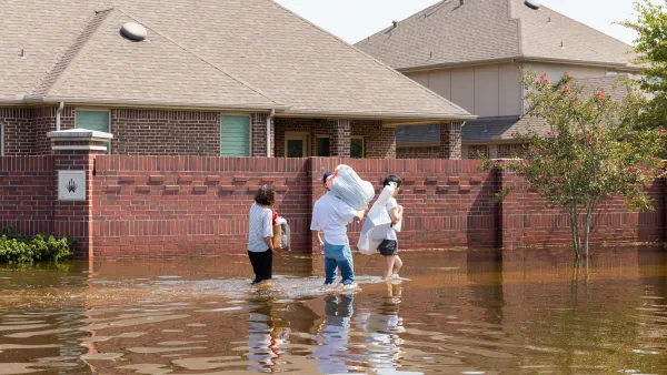 Family walking through knee-high flood waters next to brick homes in Houston, Texas.