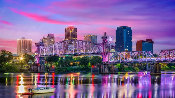 Downtown Little Rock, Arkansas skyline visible over river with steel bridge at dusk with colorful reflections on the water.