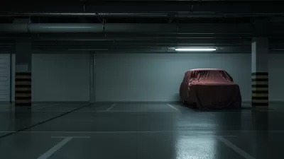 Dark parking garage, empty except for one car covered with a red tarp