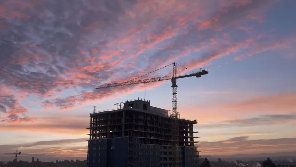 Construction crane next to large building under construction against sunset sky in Seattle, Washington.