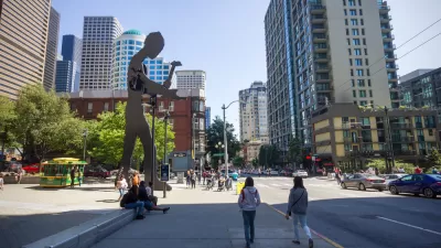 People walking on a sidewalk in front of the Seattle Art Museum, which have the hammering man and a skyscraper in the background, Washington, USA