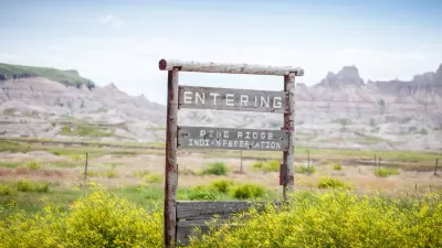 Wooden roadside sign "Entering Pine Ridge Indian Reservation" with mountains in background