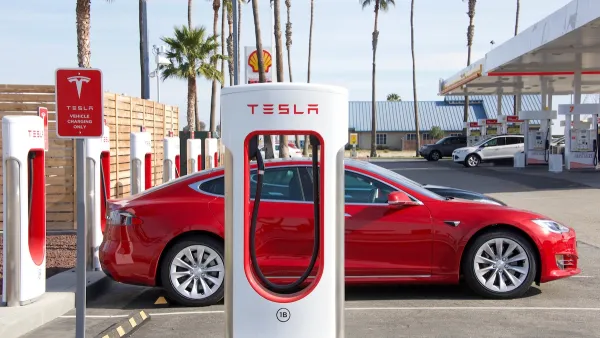 Red Tesla car parked at a Tesla charger at a gas station on a sunny day.
