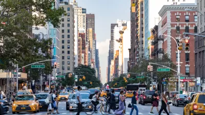 Pedestrians crossing a busy crosswalk on New York City street with tall buildings in background