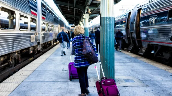 Passengers pulling roller bags on outdoor train platform between trains.