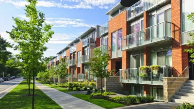 Row of modern red brick townhomes on street with sidewalk and young trees