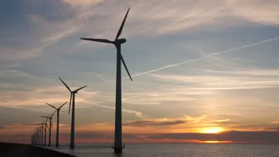 Line of offshore wind turbines with sunset over sea in the background