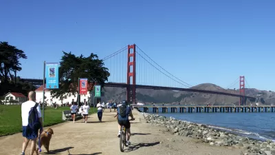 People walking and biking on flat dirt trail next to San Francisco Bay with Golden Gate Bridge in background